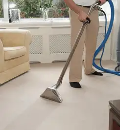 Professional carpet cleaner using a hot-water extraction wand and hose machine in a living room in Wichita, KS.