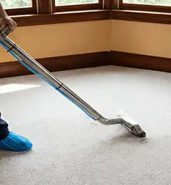 Steam carpet cleaning technician using a hot-water extraction wand on a residential carpet, wearing blue protective shoe covers Wichita, KS.