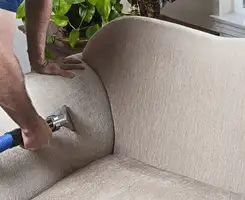 Professional upholstery cleaner deep-cleaning a fabric sofa with a handheld extraction tool and hose in Wichita, KS.